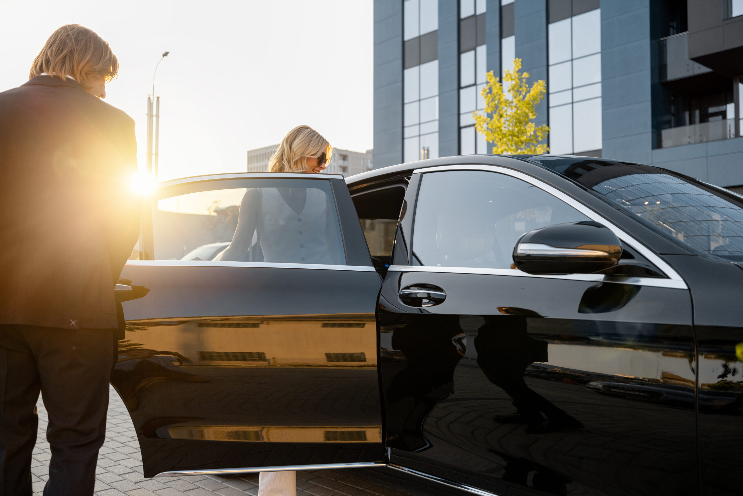 Executive black car service with a private driver assisting a client into a luxury vehicle for premium transportation.