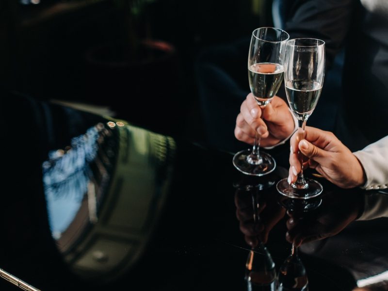 Two clients toasting with champagne inside a luxury black car, highlighting high-end chauffeur services.